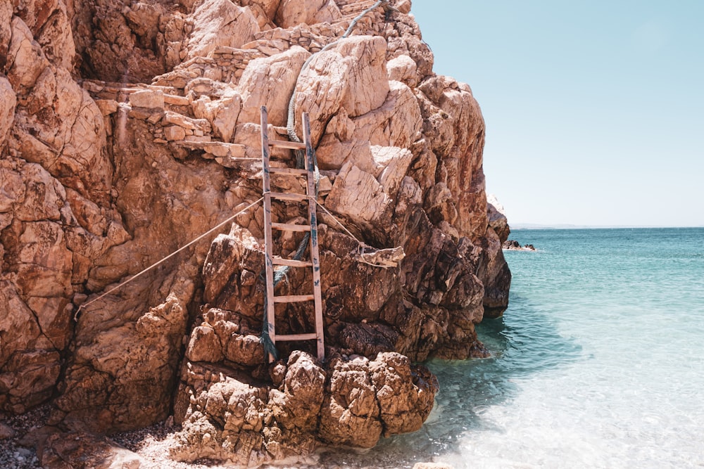 brown wooden ladder on brown rock formation near body of water during daytime