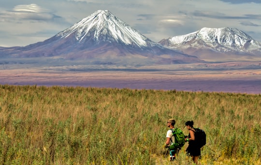 man and woman sitting on grass field near mountain during daytime in El Loa Chile