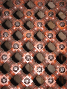 A detailed view of a lattice pattern composed of interlocking wooden beams with circular metal bolts at each intersection, creating a geometric and symmetrical design.
