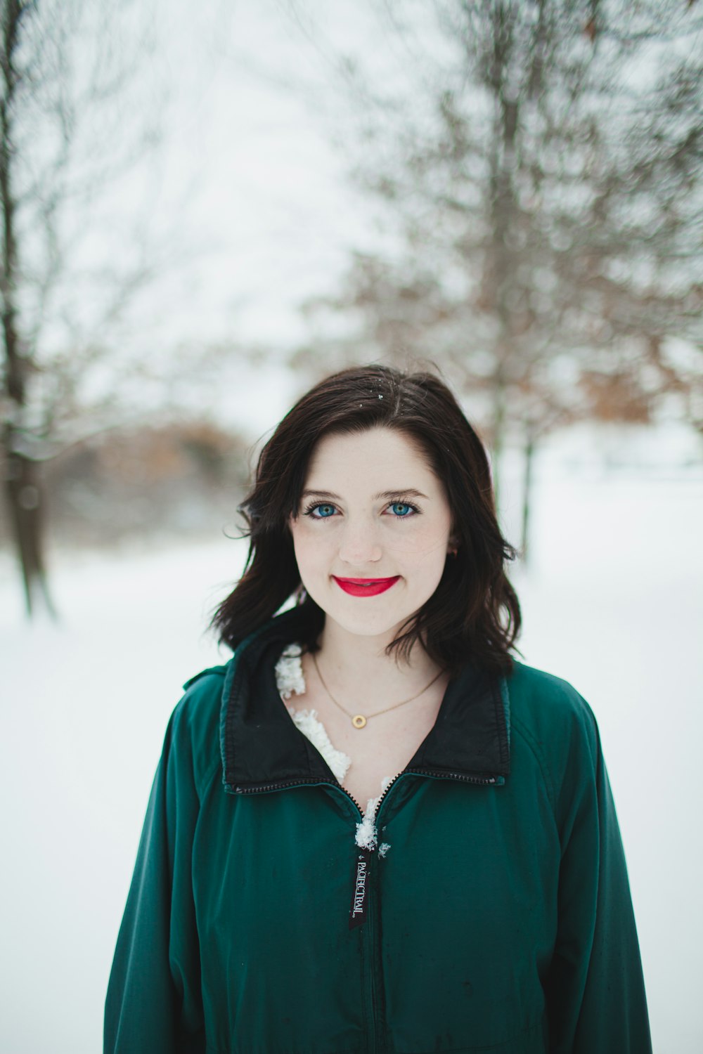 woman in green zip up jacket standing near bare trees during daytime