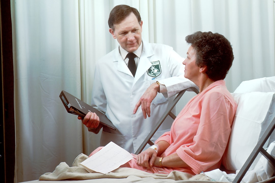 A Caucasian male doctor from the Oncology Branch consults with a Caucasian female adult patient, who is sitting up in a hospital bed.