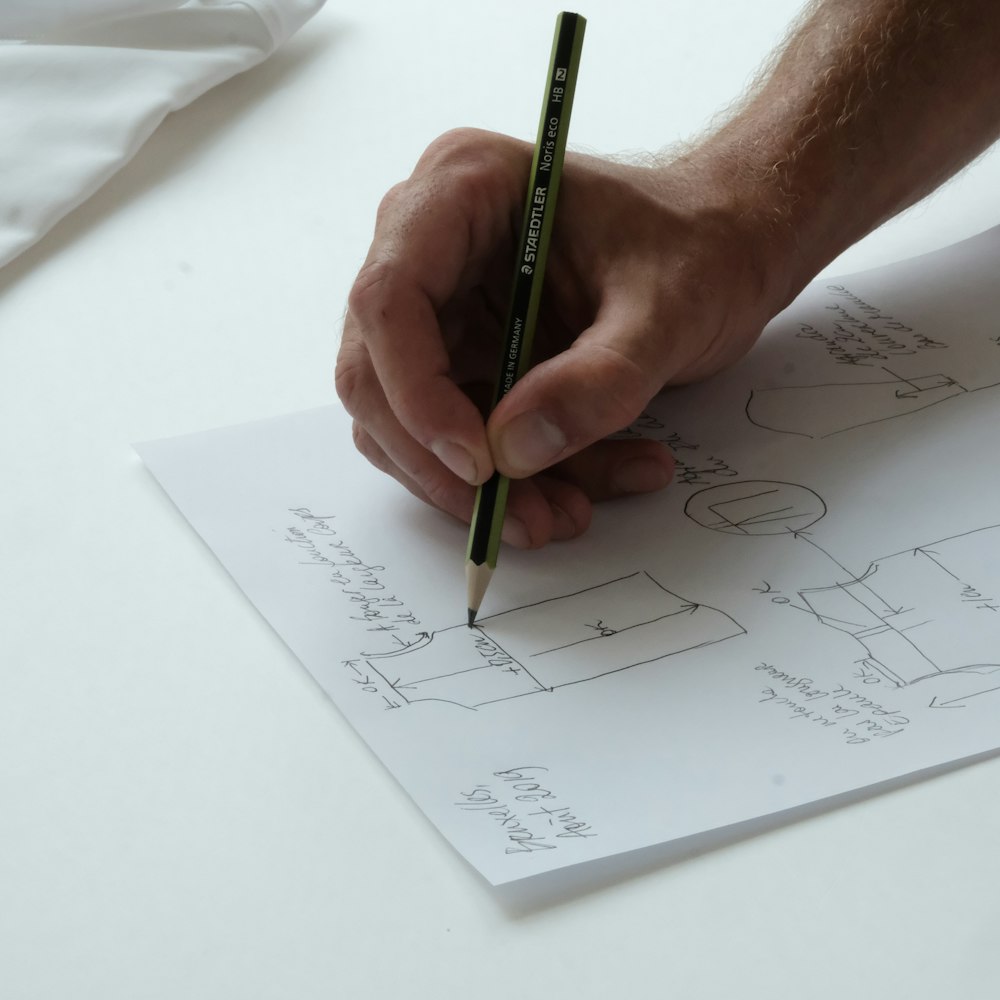 person holding black pencil on white printer paper