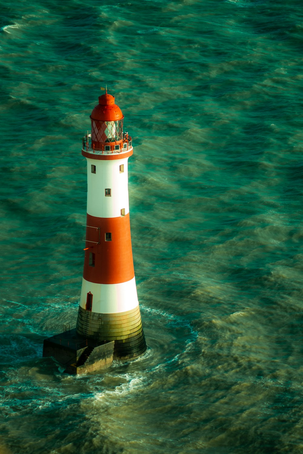 Weißer und roter Leuchtturm auf einer Klippe neben dem Gewässer während des Tages