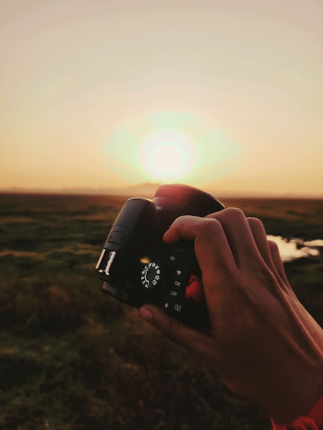 A candid shot of a photographer adjusting camera settings against a sunset backdrop.
