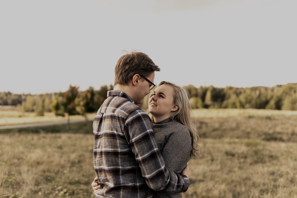 man in black sweater hugging woman in plaid shirt