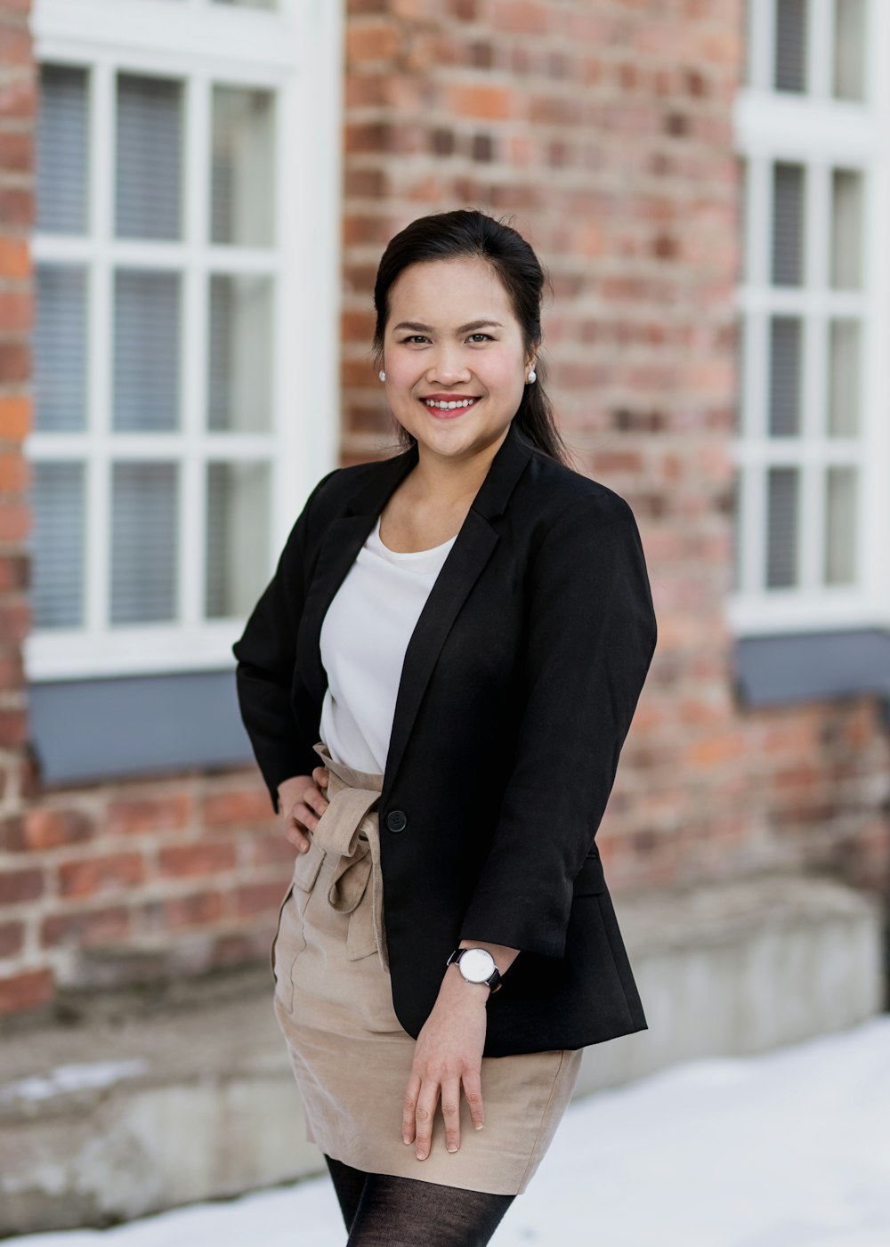 woman in black blazer and beige skirt standing near brown brick wall during daytime