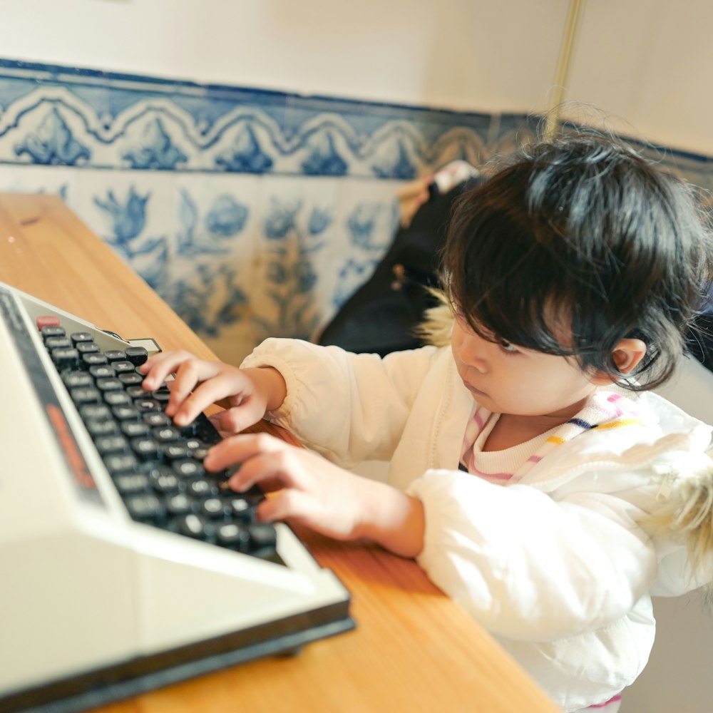 child in white long sleeve shirt using macbook pro