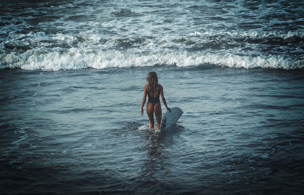 昼間、海の波でサーフィンする黒いビキニの女性