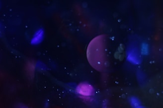 A dreamy and abstract scene featuring a dark background filled with various shades of blue and purple. A prominent spherical shape, resembling a planet, is visible in the center, surrounded by specks of light that appear like stars or cosmic dust.