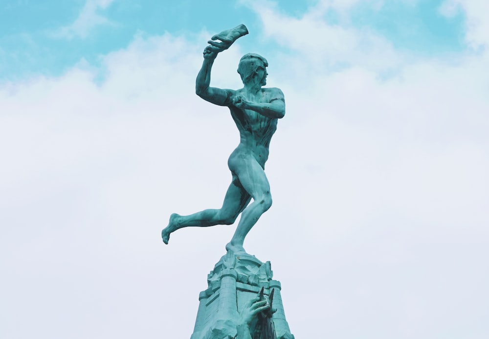 statue of man holding book under white clouds during daytime