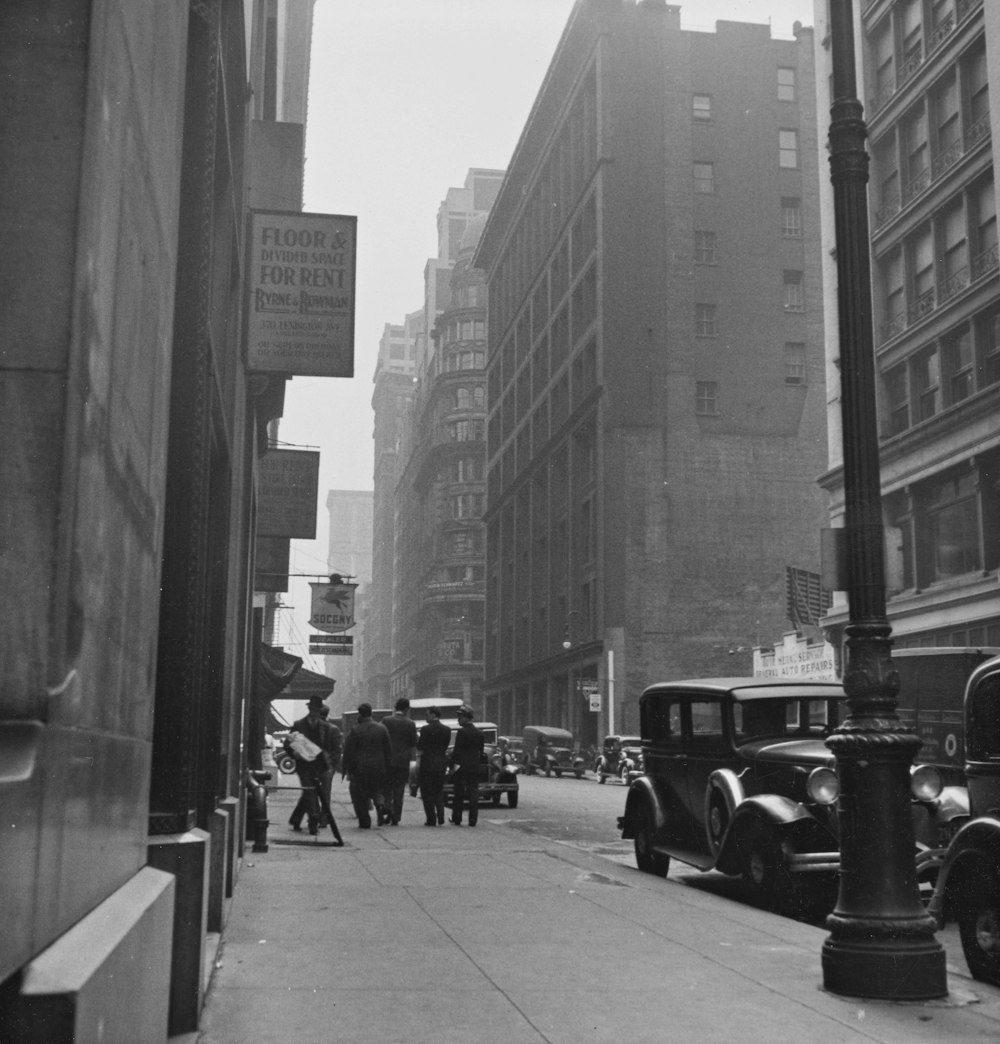 grayscale photo of people walking on sidewalk near buildings