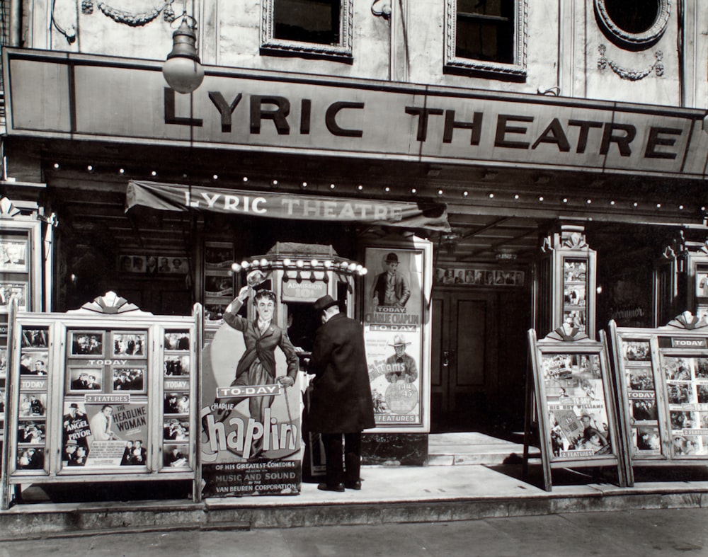 grayscale photo of man standing in front of store