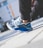 A close-up view of a person wearing stylish sneakers with a modern design, featuring a mix of blue, white, and black colors. The person is crouching, and the background is slightly blurred, suggesting an urban setting.