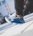 A close-up view of a person wearing stylish sneakers with a modern design, featuring a mix of blue, white, and black colors. The person is crouching, and the background is slightly blurred, suggesting an urban setting.