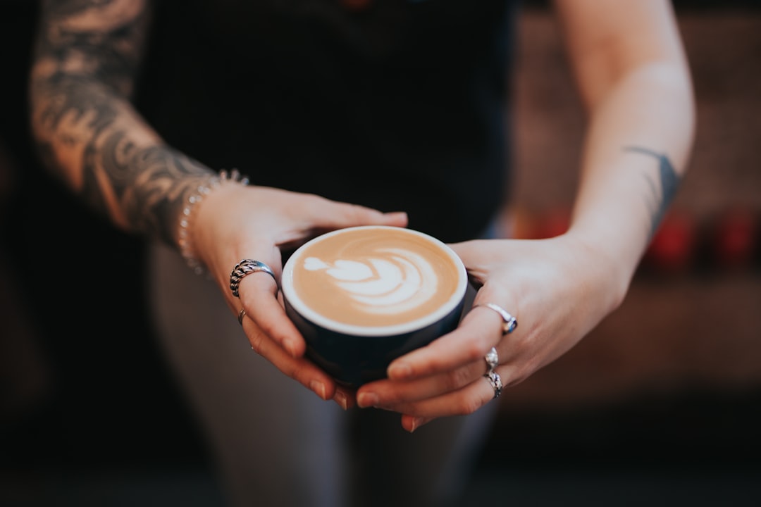 person holding white ceramic cup with cappuccino