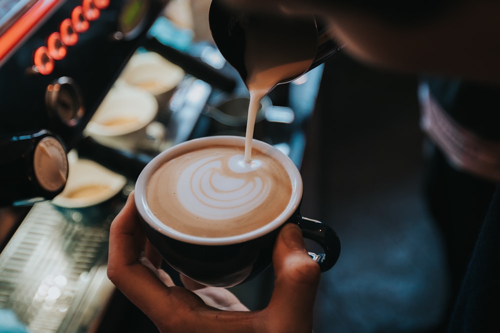 person pouring coffee on black ceramic mug