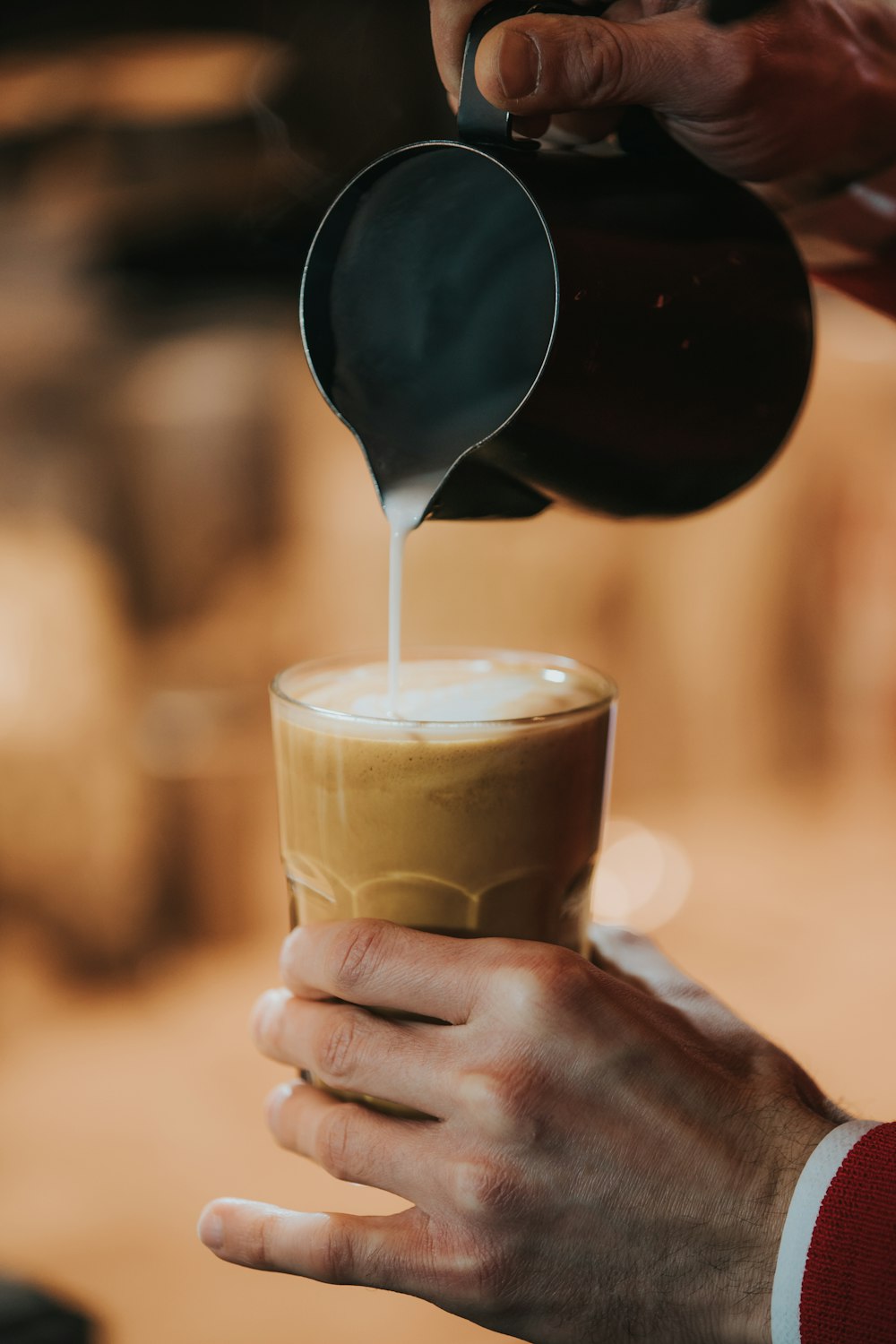 person holding clear drinking glass with brown liquid