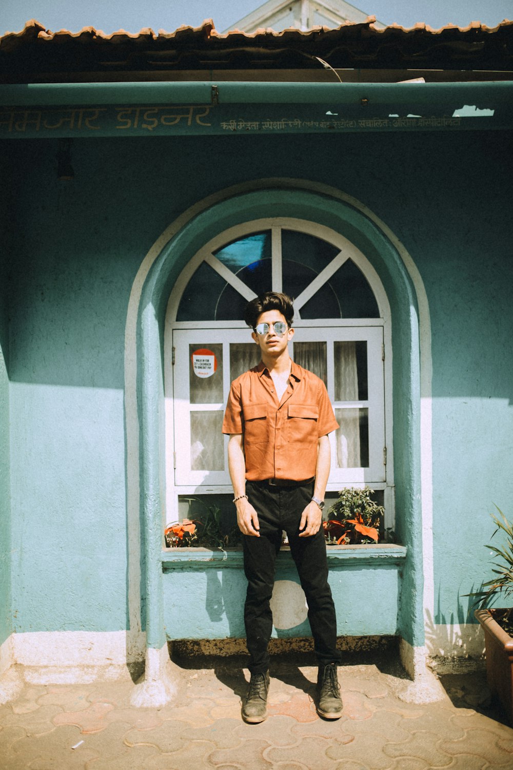 man in brown button up shirt and black pants standing beside blue wooden door