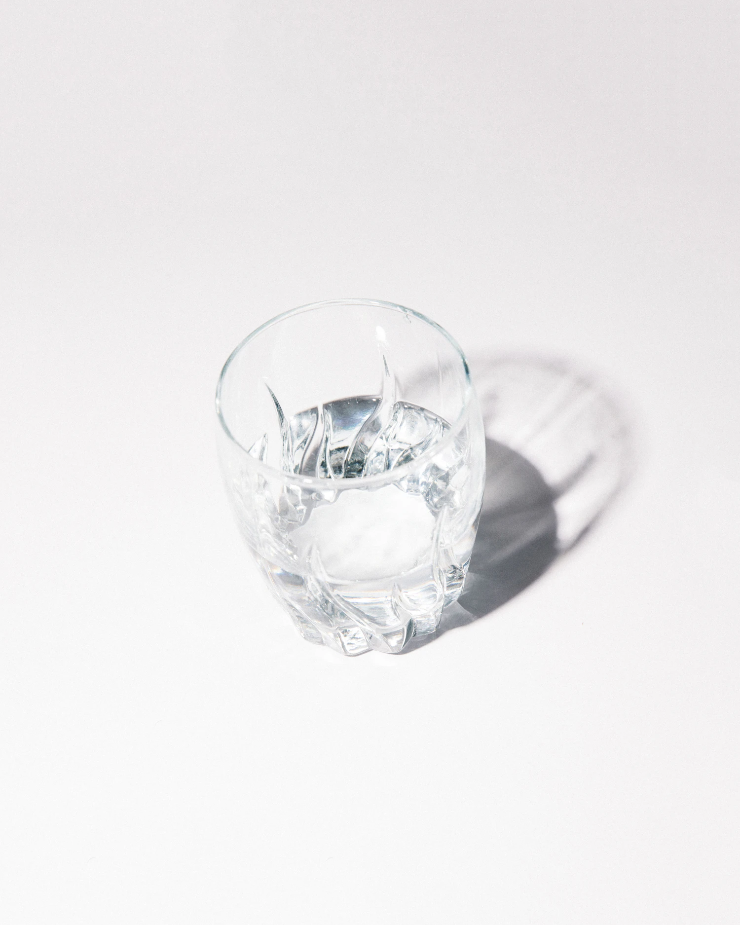 A cut-crystal rocks glass of water on white, its facets casting a soft shadow