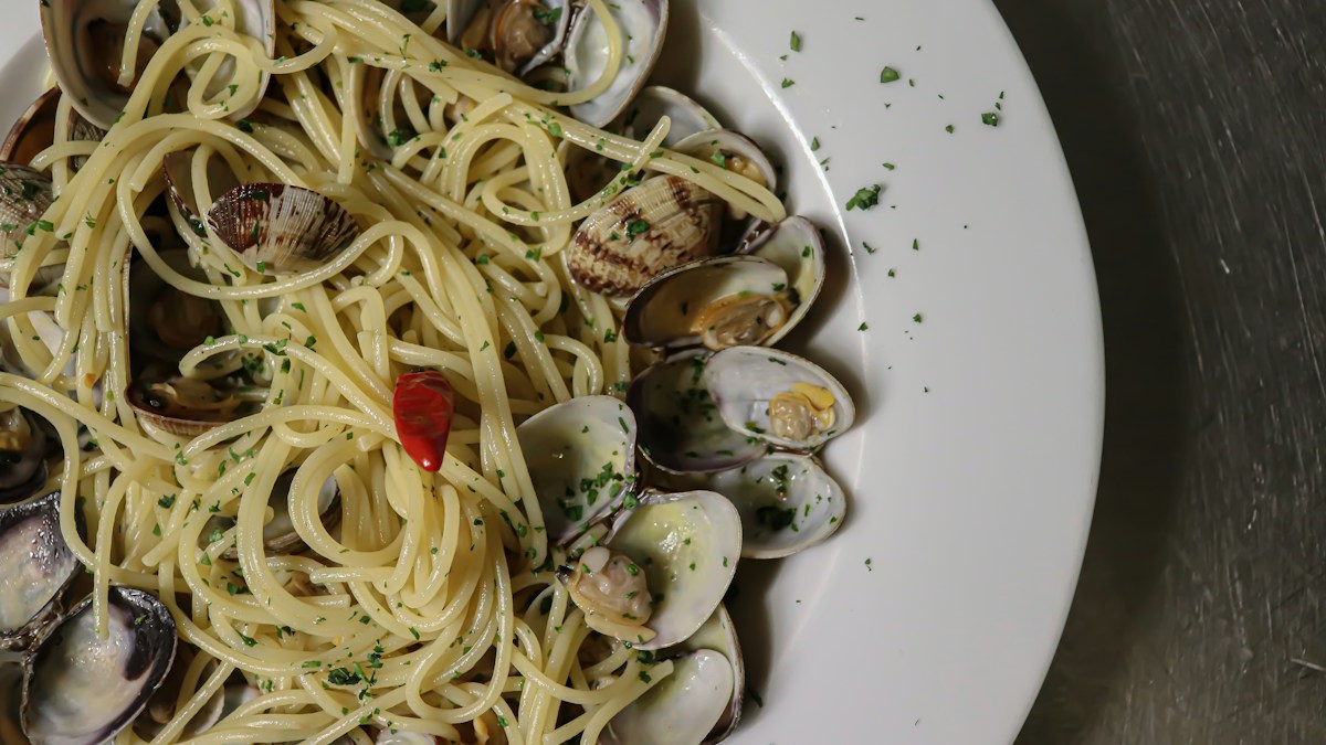 Assiette de spaghetti aux palourdes parsemés de persil, avec un morceau de piment rouge