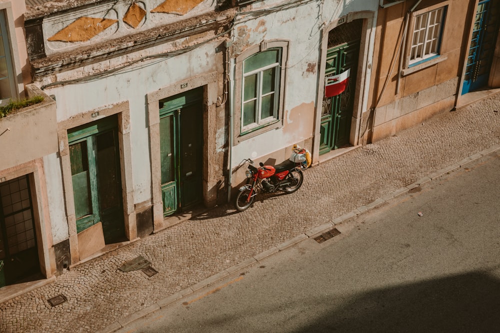 red motorcycle parked beside brown concrete building during daytime
