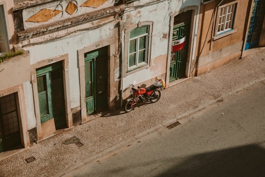 red motorcycle parked beside brown concrete building during daytime in Faro Portugal
