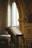 An ornate wooden lectern holds an open, aged book inside a dimly-lit, classical architectural setting with decorative arches and columns.