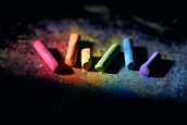 Close-up of a child's hands holding colorful chalks on an orange and green background.