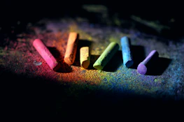 Close-up of a child's hands holding colorful chalks on an orange and green background.