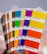 A hand holds a fanned-out selection of Pantone color swatches. The swatches include a variety of vibrant colors, such as pink, yellow, green, blue, orange, and red. The background is softly blurred, enhancing the focus on the colorful swatches.
