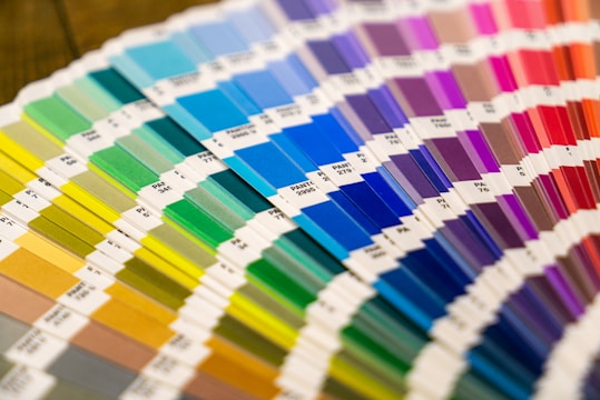 A collection of color swatches arranged in a fan shape, showcasing a wide range of hues from green to purple to red. Each swatch is labeled with specific color codes.