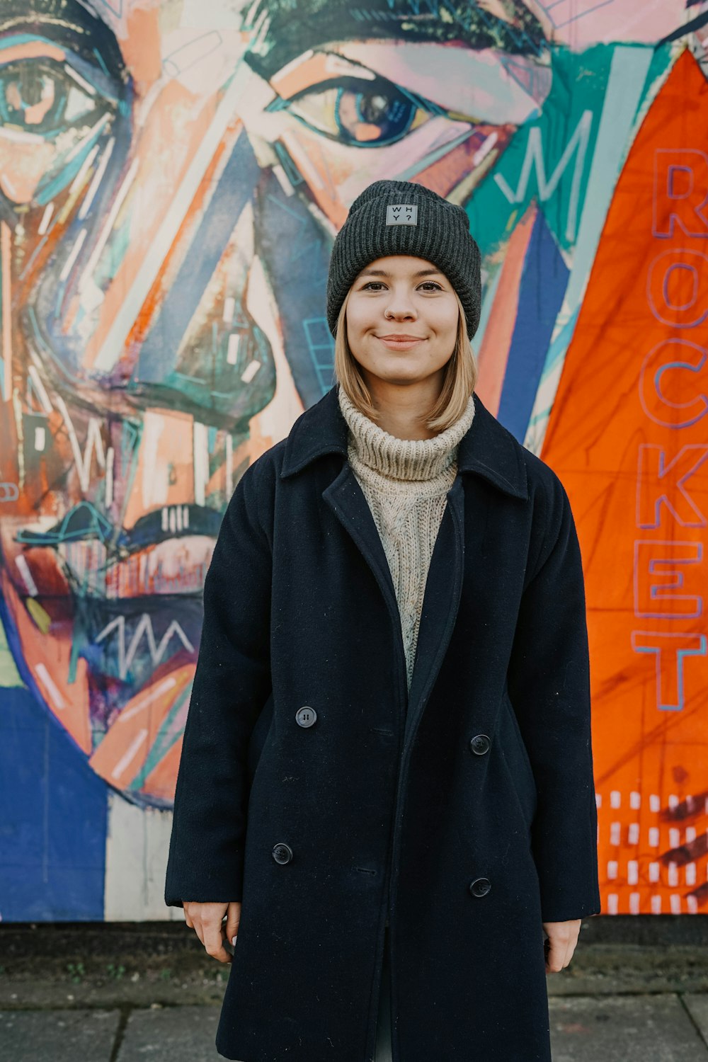 woman in black coat standing near graffiti wall