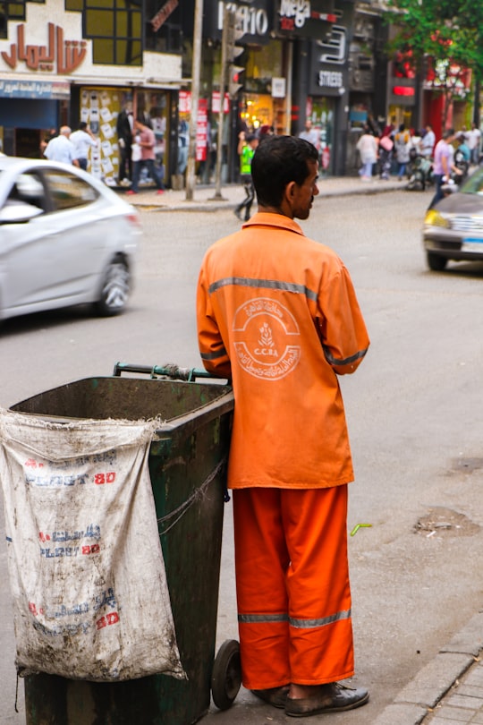 man in orange long sleeve shirt and red pants standing on sidewalk during daytime in Downtown Cairo Egypt