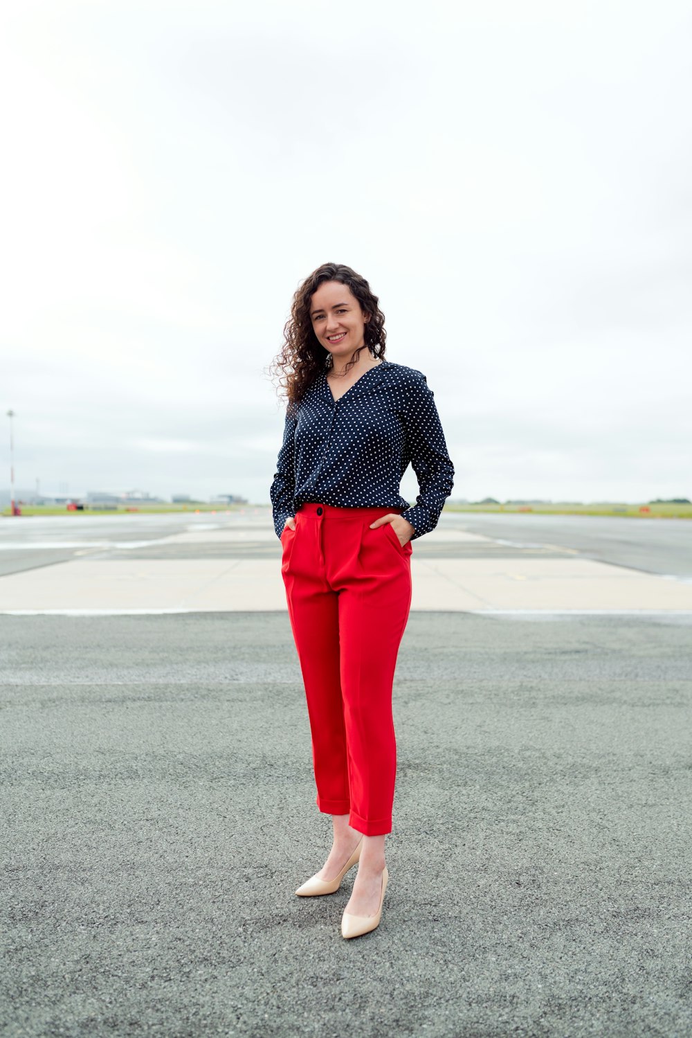 woman in black and white polka dot long sleeve shirt and red pants standing on gray