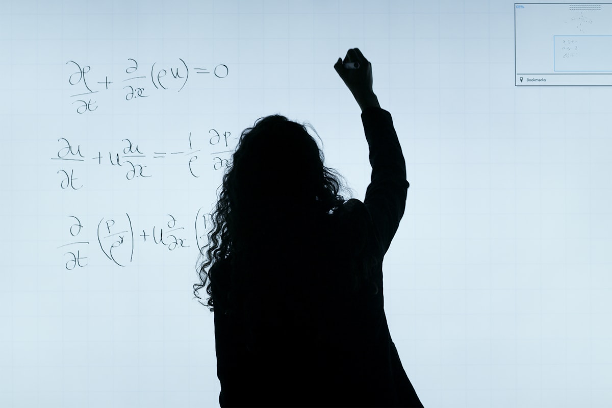 Silhouette of a person with long hair writing equations on a whiteboard with their right h