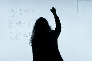 A person stands in front of a whiteboard writing mathematical equations. The silhouette is visible against the softly illuminated board filled with handwritten mathematical expressions.
