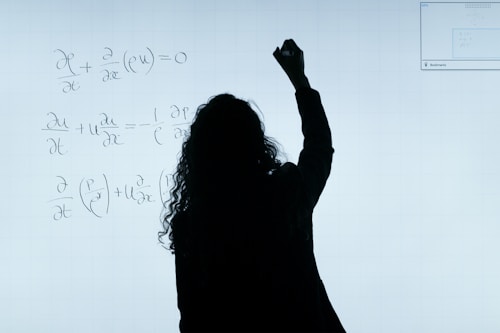 A person stands in front of a whiteboard writing mathematical equations. The silhouette is visible against the softly illuminated board filled with handwritten mathematical expressions.