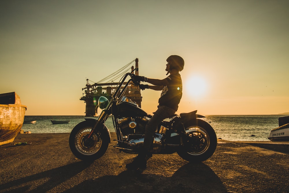 homem que monta a motocicleta na praia durante o pôr do sol