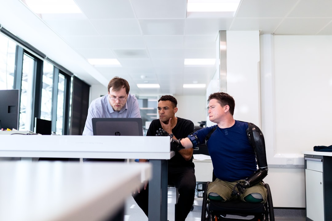 man in blue dress shirt sitting on black office rolling chair, Engineers look at computer screen with prosthetic limb user
