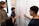 A group of four people are engaged in a collaborative discussion around a whiteboard covered in mathematical equations and graphs drawn in red marker. They appear attentive and focused, with one person actively explaining or discussing the content on the board.