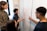 A group of four people are engaged in a collaborative discussion around a whiteboard covered in mathematical equations and graphs drawn in red marker. They appear attentive and focused, with one person actively explaining or discussing the content on the board.
