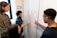 A group of four people are engaged in a collaborative discussion around a whiteboard covered in mathematical equations and graphs drawn in red marker. They appear attentive and focused, with one person actively explaining or discussing the content on the board.