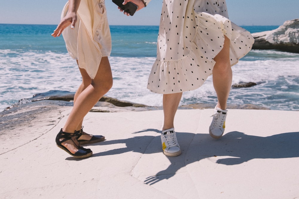 woman in yellow and white polka dots dress and white shoes standing on beach during daytime