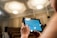A person is holding a tablet with a digital drawing displayed on it. The setting appears to be an auditorium with empty seating in the background and a bright, well-lit ceiling above. The person is likely using the tablet to create or view architectural designs.