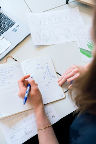 Close-up of hands writing notes during a coaching session, blue pen on white paper with a laptop nearby
