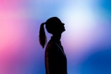 A silhouette of a person with a ponytail, facing upwards against a vibrant gradient background of pink and blue hues.