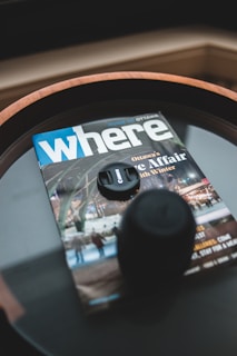 A magazine with a cover title 'where' and a subtitle 'Ottawa's Ice Affair with Winter' lies on a table. A camera lens cap and what seems to be a lens or cup are placed on top of it. The cover image of the magazine displays a winter theme with people and lights.