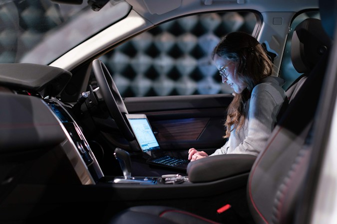 A passenger seated in a vehicle without touching the steering wheel, similar to riding in a driverless robotaxi