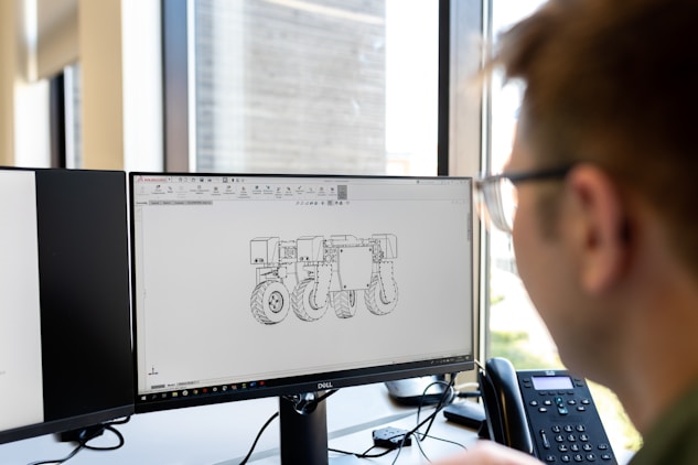 Engineer viewing mechanical engineering CAD drawing of agricultural equipment on a dual-monitor work