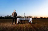 A young farmer using a tablet in the middle of a vast agricultural landscape.